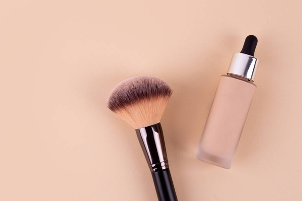 Liquid foundation cream unbranded bottle with makeup brush. Facial correction, liquid concealer, tone, bb, cc cream skincare product on beige background. Feminine cosmetics accessory with copy space - Fotoğraf, Görsel
