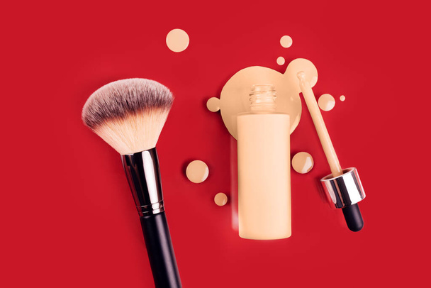 Spilled liquid foundation. Mockup glass bottle of correction cosmetic product with pipette and brush for make up on red background. beauty branding concept - Photo, image
