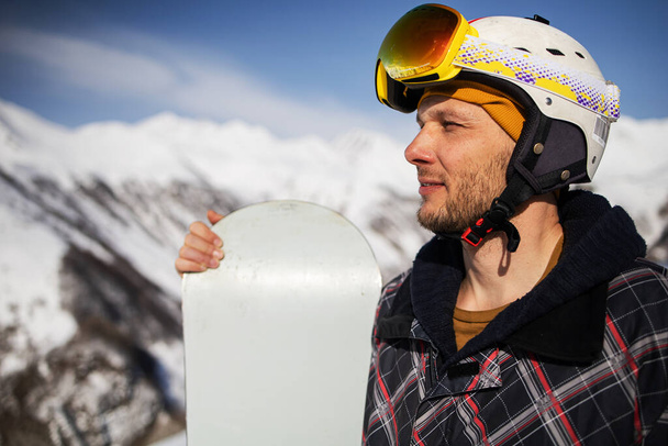 Close-up portrait of a skier in a mask and helmet against a background of snow-capped mountains and blue sky - Photo, Image