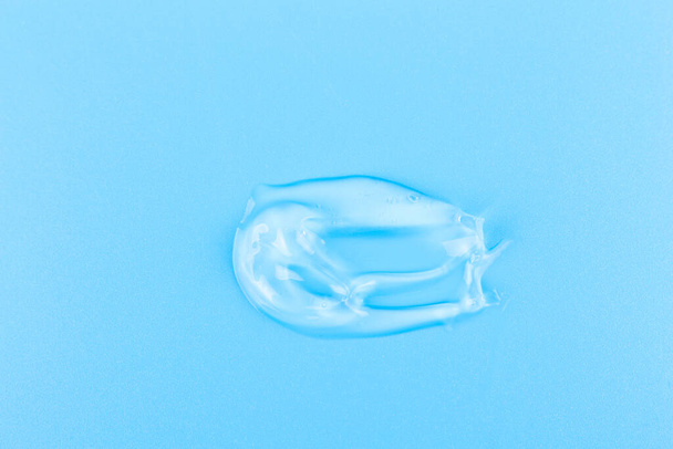 Smear of cosmetology transparent product for face treatment. Drop of cream on blue background. Lotion or mask. Beauty wellness and professional skincare concept. - Фото, зображення