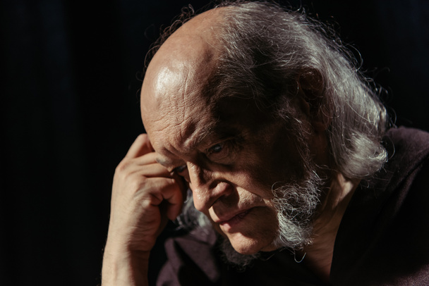 anziano filosofo religioso che tiene la mano vicino alla testa piegata mentre pensa isolato su nero - Foto, immagini
