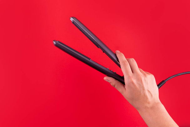 Millennial woman holding hair straightener on red background, closeup. Panorama. Modern hair iron for straightening - Foto, immagini