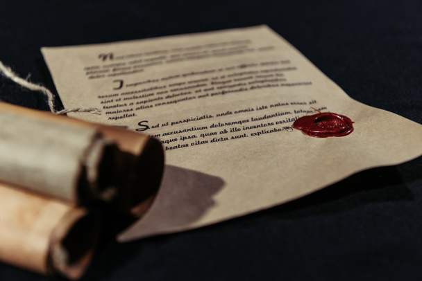 manuscrito carimbado com selo de cera perto de pergaminhos laminados em fundo preto - Foto, Imagem