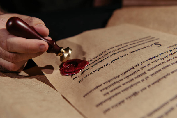 cropped view of monk with wax seal near ancient manuscript isolated on black - Fotoğraf, Görsel