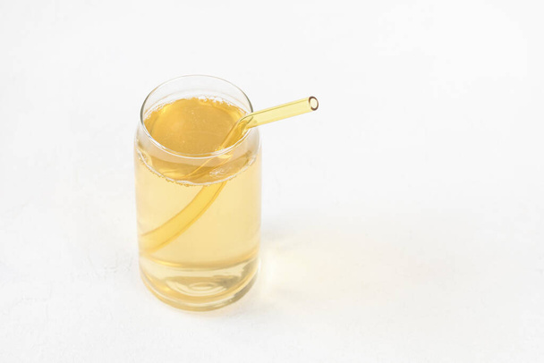 Homemade kombucha fermented drink in glass and colored reusable eco-friendly straw on white background. Heathy probiotic beverage with bubbles. Summer non alcoholic drinks. Copy space - 写真・画像