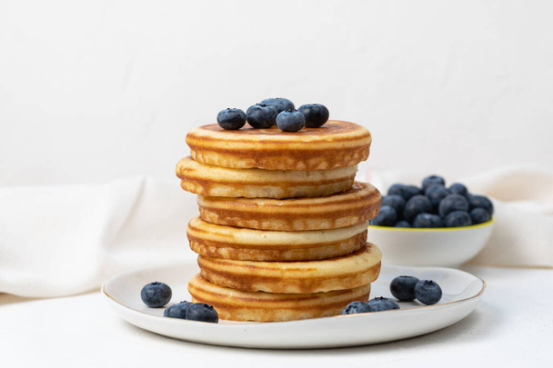 Stack of delicious pancakes on white plate with fresh blueberries on and in bowl. Side view, Copy space - 写真・画像