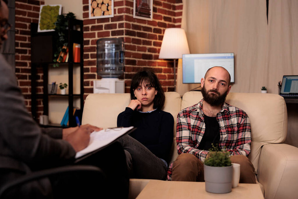 Portrait of unhappy couple talking to counselor at therapy session, trying to solve relationship difficulties together with therapist. Dealing with marriage problems at counseling support. - Photo, Image
