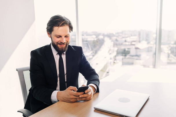 Happy businessman using telephone mobile corporate applications at workplace, sending sms, man looking at smartphone browsing internet, office technology and digital communication - Foto, Imagen