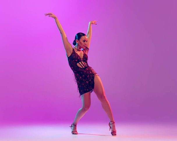 Smoothness and accuracy of movements. Young graceful flexible woman dancing ballroom dance without partner isolated on purple background. Concept of art, timeless, beauty, music, style - Foto, Bild