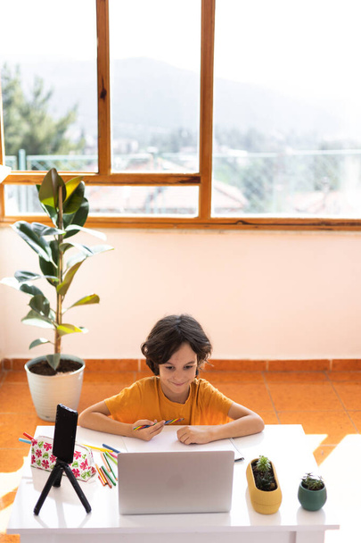 παιδί αγόρι χρησιμοποιεί ένα φορητό υπολογιστή και να μελετήσει σε απευθείας σύνδεση με το δάσκαλο κλήση βίντεο στο σπίτι, κατ 'οίκον διδασκαλία, εξ αποστάσεως εκπαίδευση, online εκπαίδευση, το παιδί σε απευθείας σύνδεση μάθημα, εξ αποστάσεως εκπαίδευση - Φωτογραφία, εικόνα