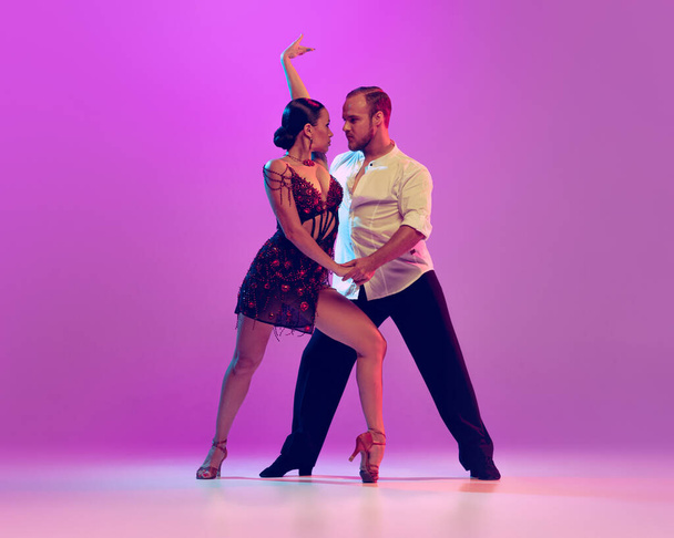 Energy and expression. Beautiful coupleof dancers in adorable attires dancing ballroom dance isolated on purple background. Concept of art, dance, beauty, music, style. Copy space for ad - Photo, image