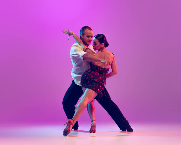 Elegance. Two young graceful dancers wearing stage outfits dancing ballroom dance isolated on purple background. Concept of art, dance, beauty, music, style. Copy space for ad - Φωτογραφία, εικόνα