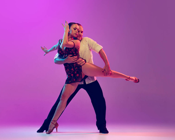 Passion, love, support. Young man and woman, ballroom dancers in motion isolated on purple background. Concept of art, dance, beauty, music, style. Copy space for ad. International Dance Day - Foto, Imagen