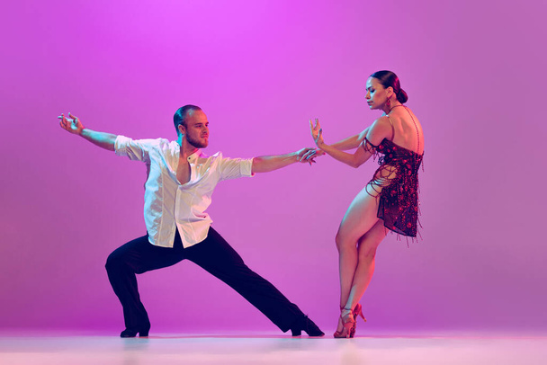Passion, love, support. Young man and woman, ballroom dancers in motion isolated on purple background. Concept of art, dance, beauty, music, style. Copy space for ad. International Dance Day - Zdjęcie, obraz