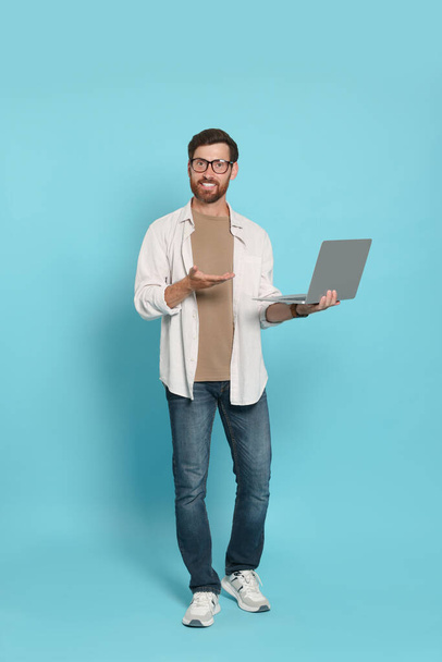 Handsome man with laptop on light blue background - Foto, imagen