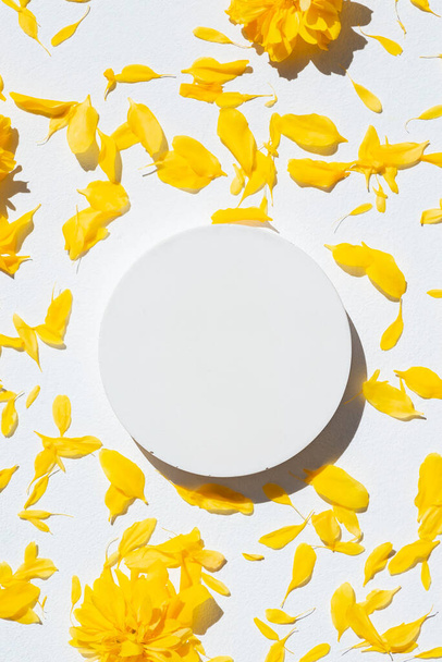 White podium for product presentation on yellow flower petals background. Empty cylindrical platform for cosmetic. Mockup with concrete circle and copy space. - Foto, Imagen