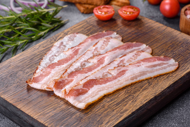 Raw smoked bacon on a wooden board with several cut pieces - Foto, afbeelding