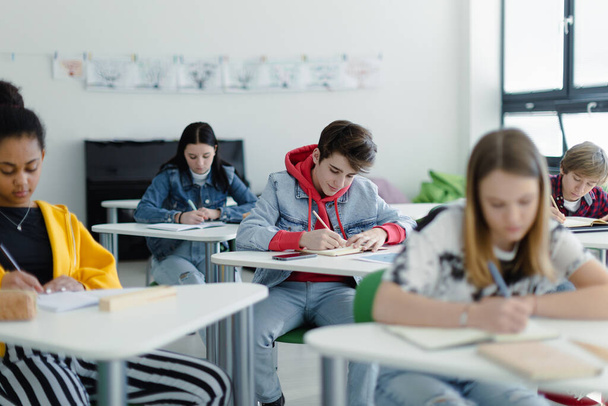 Estudiantes de secundaria prestando atención en una clase, sentados en sus escritorios y notas de escritura, de vuelta al concepto escolar. - Foto, imagen