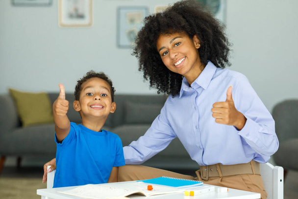 Image of a young female teacher showing thumbs up along with her student sitting in a classroom . High quality photo - Foto, Bild