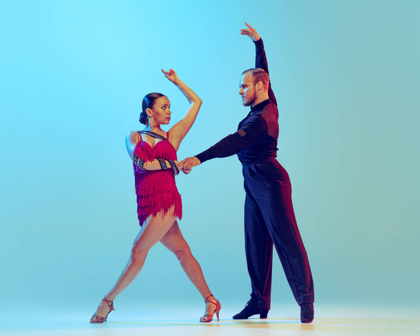 Paso doble. Studio shot of young couple, professional dancers dancing ballroom dance isolated on blue background. Concept of art, dance, beauty, music, style. Copy space for ad. International Dance - Fotografie, Obrázek