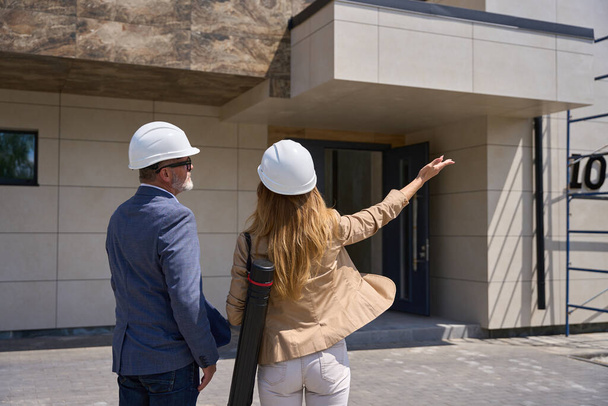 Realtor woman shows a new house to a client. They stand on the street in front of the entrance. Back view - Φωτογραφία, εικόνα