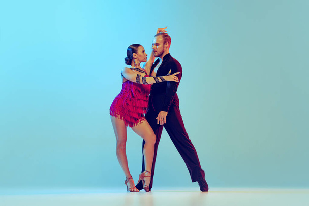 Paso doble. Studio shot of young couple, professional dancers dancing ballroom dance isolated on blue background. Concept of art, dance, beauty, music, style. Copy space for ad. International Dance - Foto, Imagem