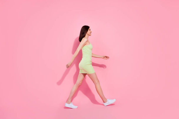 Full length photo of sweet shiny young lady wear green dress walking empty space isolated pink color background. - Photo, Image