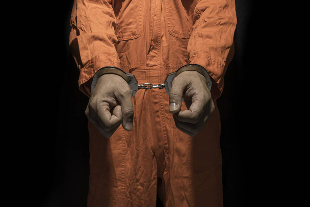 Handcuffs on Accused Criminal in Orange Jail Jumpsuit. Law Offender Sentenced to Serve Jail Time, in black background - 写真・画像