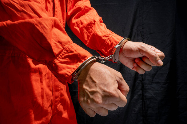 Handcuffs on Accused Criminal in Orange Jail Jumpsuit. Law Offender Sentenced to Serve Jail Time, in black background - Zdjęcie, obraz