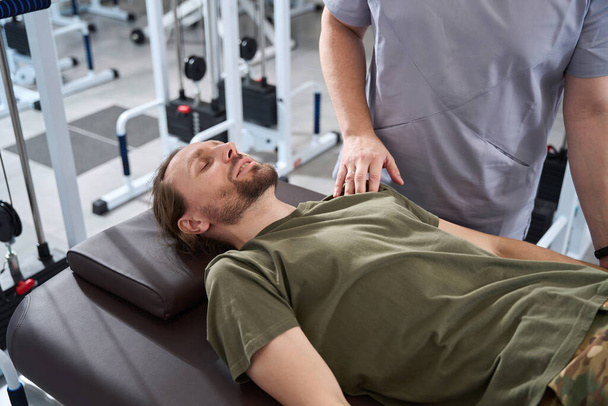 Soldier in military clothes lies on a massage table in a rehabilitation center, specialist in therapeutic massage works with him - Foto, afbeelding