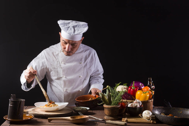 Male chef in white uniform prepares spaghetti with vegetables on the dish before serving while working in a restaurant kitchen - Photo, Image