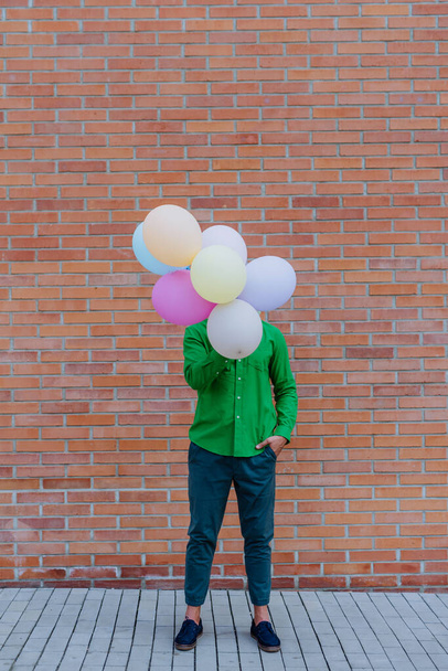 Zábavný portrét šťastného, energického dospělého muže držícího balónky na ulici a skrývajícího se za nimi, který se cítí volný. - Fotografie, Obrázek