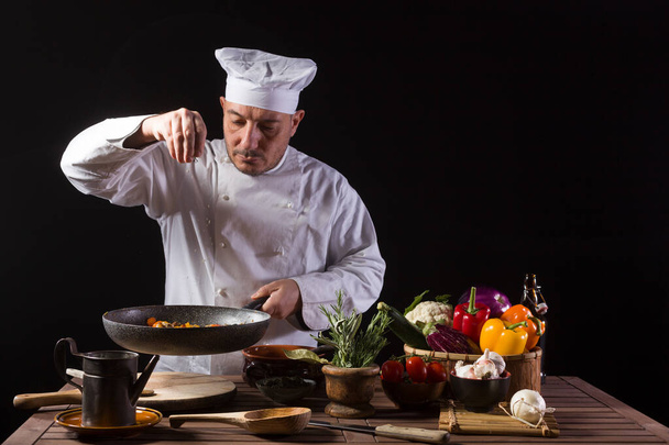 Чоловік готує в білій формі і капелюх кладе трави горщика на сковороду перед подачею під час роботи на кухні ресторану
 - Фото, зображення