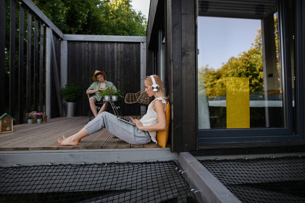 A happy young couple with laptop resting outdoors in a tiny house, weekend away and remote office concept. - Foto, Imagem