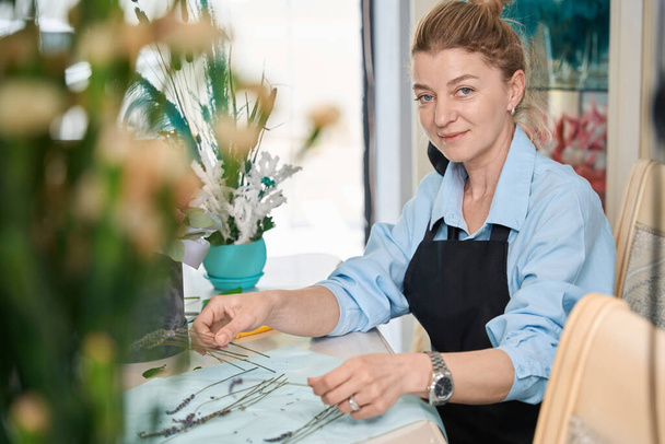 Smiling female florist with lavender in her hand, conducts online lesson on creating exclusive bouquets of flowers in box - Foto, Bild