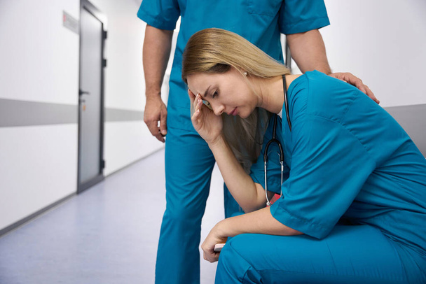Lady doctor sad sits in the corridor of the hospital holding her head - Photo, Image