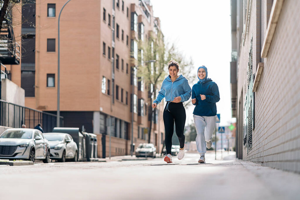 Cheerful muslim woman wearing hijab running in the street with her friend and having fun. - Foto, Bild