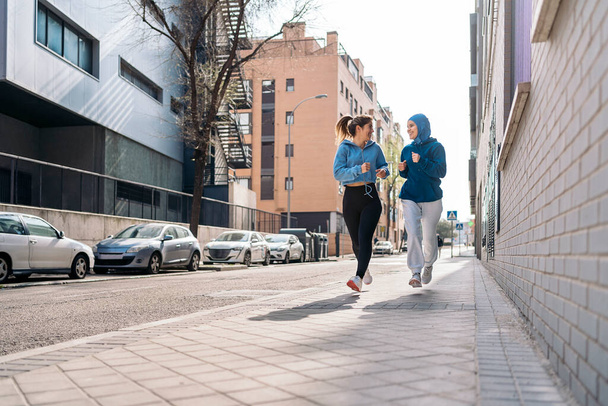 Cheerful muslim woman wearing hijab running in the street with her friend and having fun. - Фото, изображение
