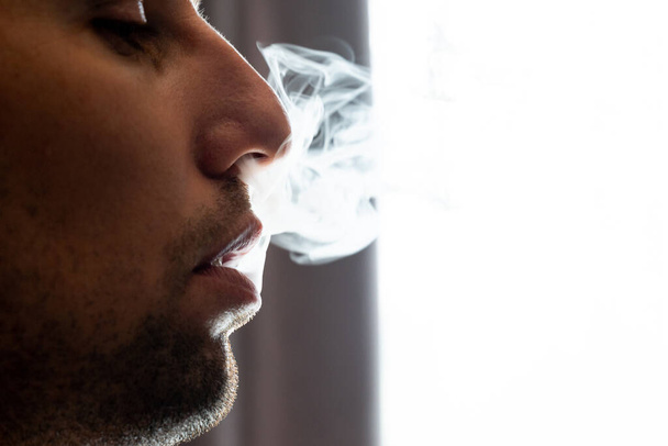 Male lips blowing smoke close-up, cigarette smoke and lips on black background, male unshaven and short beard. - Photo, Image