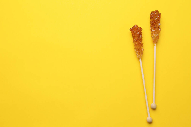 Wooden sticks with sugar crystals and space for text on yellow background, flat lay. Tasty rock candies - 写真・画像