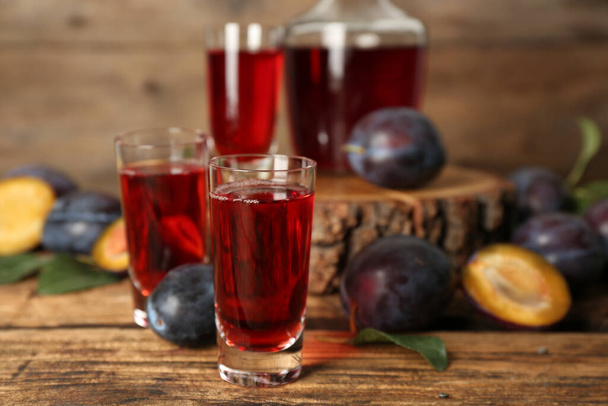 Delicious plum liquor and ripe fruits on wooden table. Homemade strong alcoholic beverage - Foto, Imagen