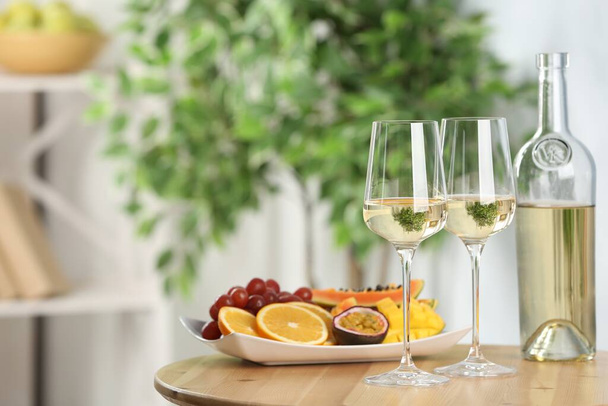 Вкусные экзотические фрукты и вино на деревянном столе в помещении, пространство для текста - Фото, изображение