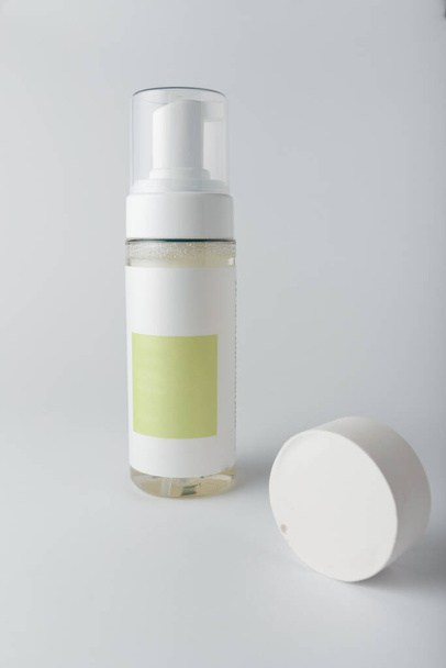 Cosméticos maqueta de plantilla, botella de espuma de lavado con etiqueta en blanco, decoración de hormigón sobre fondo blanco. Limpiador facial para el cuidado de la piel, tiro vertical - Foto, imagen