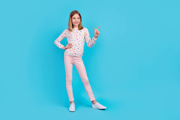 Full length photo of sweet shiny small girl wear dotted shirt looking pointing empty space isolated blue color background. - Zdjęcie, obraz