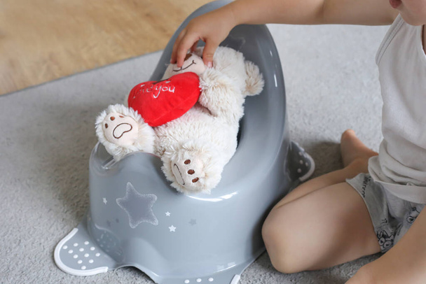 Cute baby 2 years old sits a teddy bear on the potty. Pot for children. Role play potty training - 写真・画像
