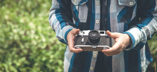 Vintage film camera in the hands of a man on a blurred background, the concept of tourism and camping. - Photo, image