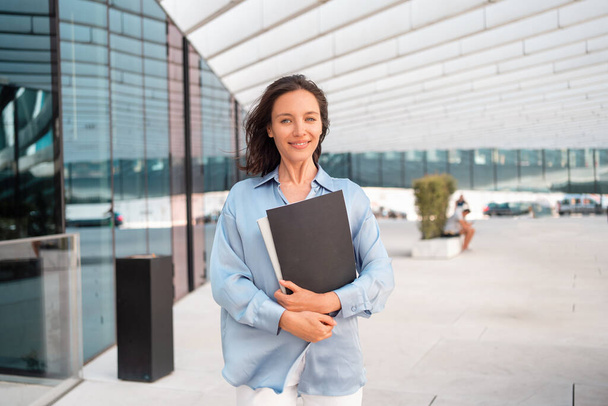 Businesswoman successful woman business person walking outdoor corporate building exterior Excited happy caucasian positive professional business female person holding folder documents Looking camera - Фото, изображение