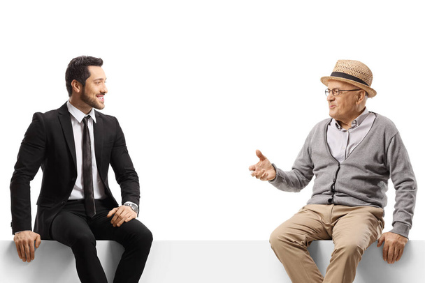 Elderly man and a young businessman sitting on a panel and talking isolated on white background - Photo, Image