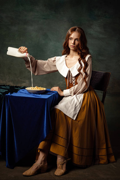 Morning traditions. Portrait of charming redhair girl with long curly hair like girl of renaissance eras isolated on dark background. Comparison of eras, beauty, history, art, creativity. - 写真・画像