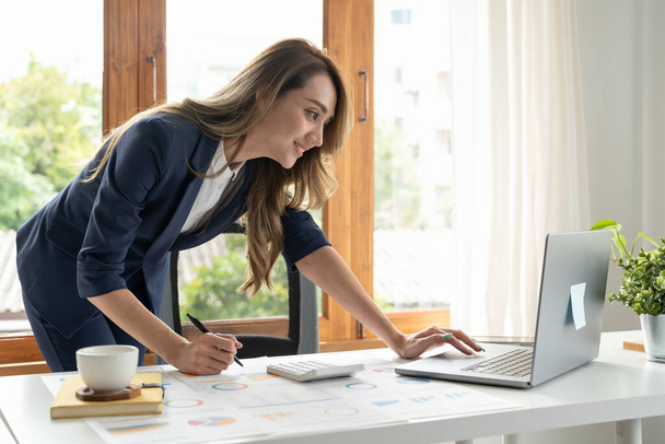 オフィスやビジネスの仕事の背景、税務、会計、統計や分析研究の概念で木製の机の上に算術ファイナンスを行うための計算機やラップトップを使用してビジネス女性. - 写真・画像